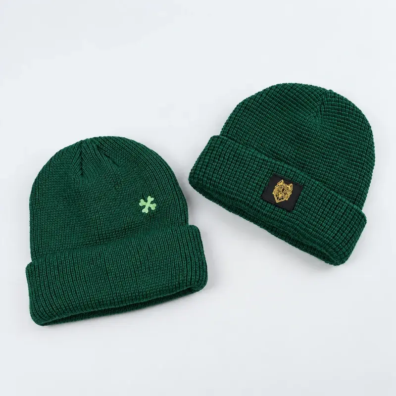 Two dark green short cuffed beanies showing different patch positions