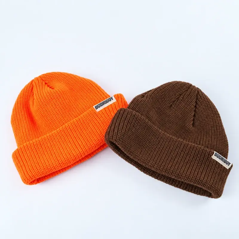 Two short cuffed beanies in orange and brown showing their crown and cuff proportions