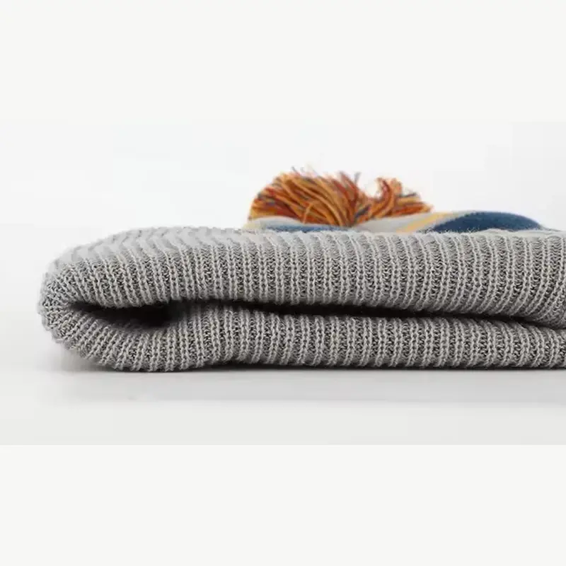 Folded gray knit cuff with multicolor yarn pom visible behind