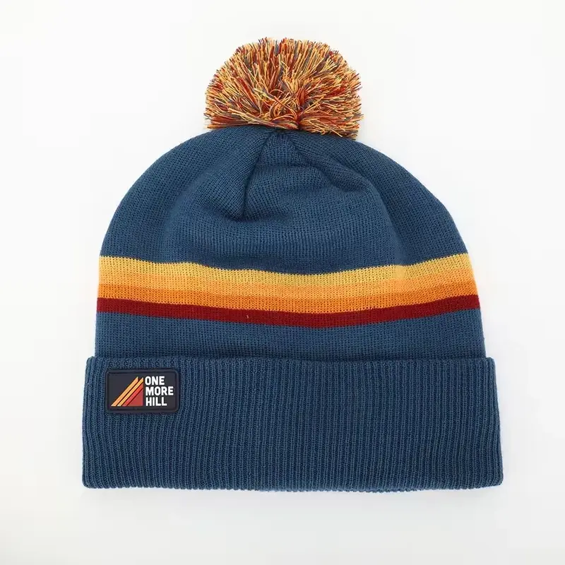 Blue striped yarn pom beanie with a small cuff patch