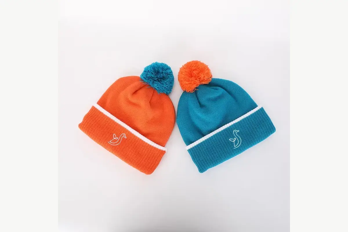 Orange and teal beanies with contrasting yarn pom colors