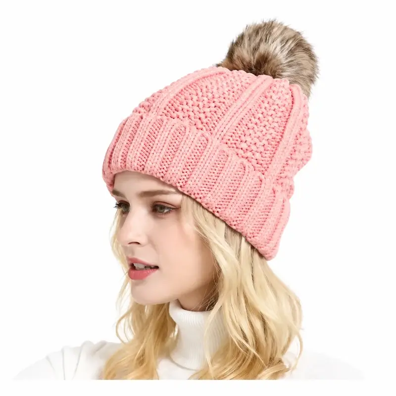 Pink cable knit beanie with a fluffy faux-fur pom-pom shown on a wearer